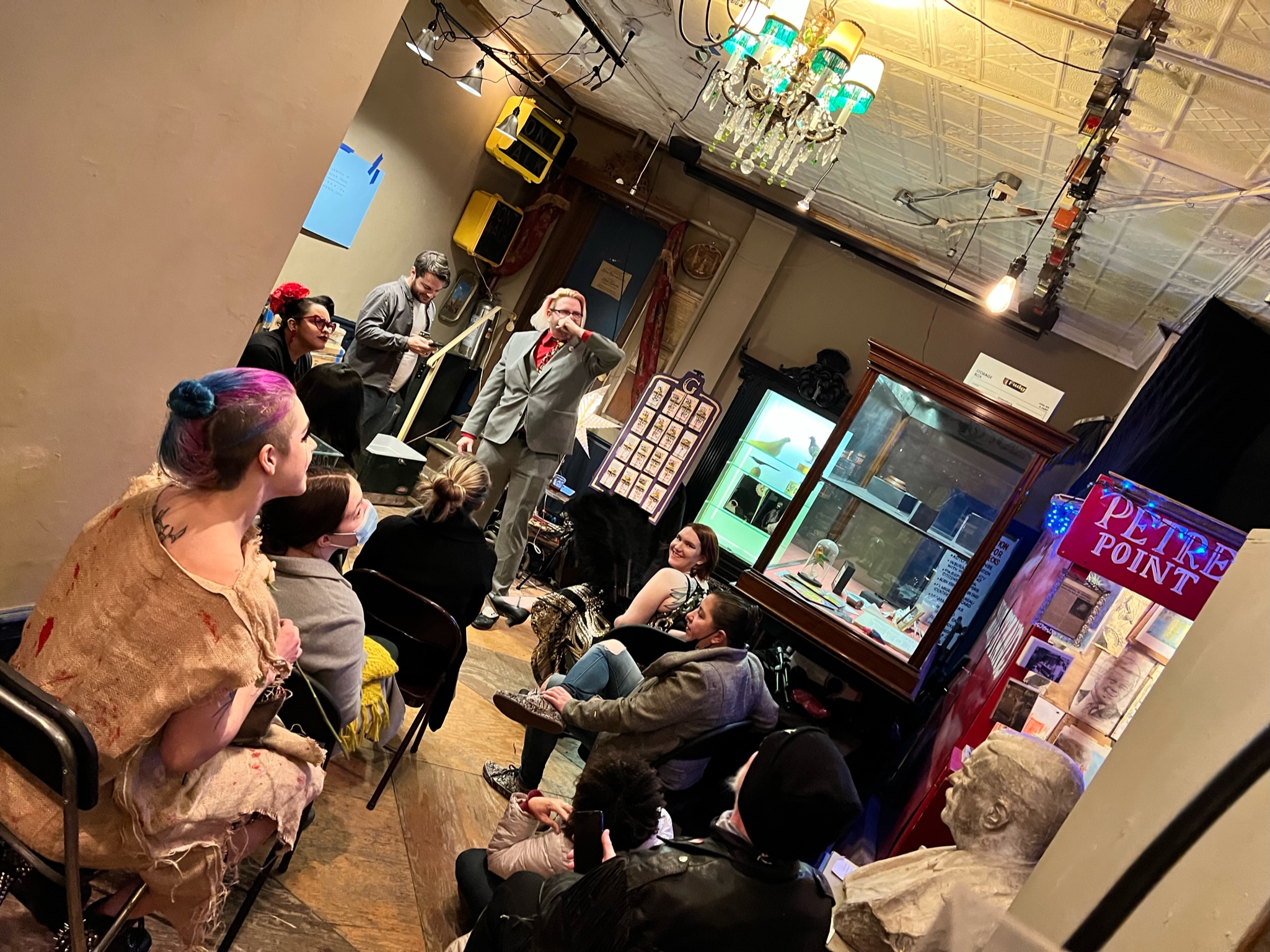 a crowd surrounded by museum artifacts is enraptured by a suited magician