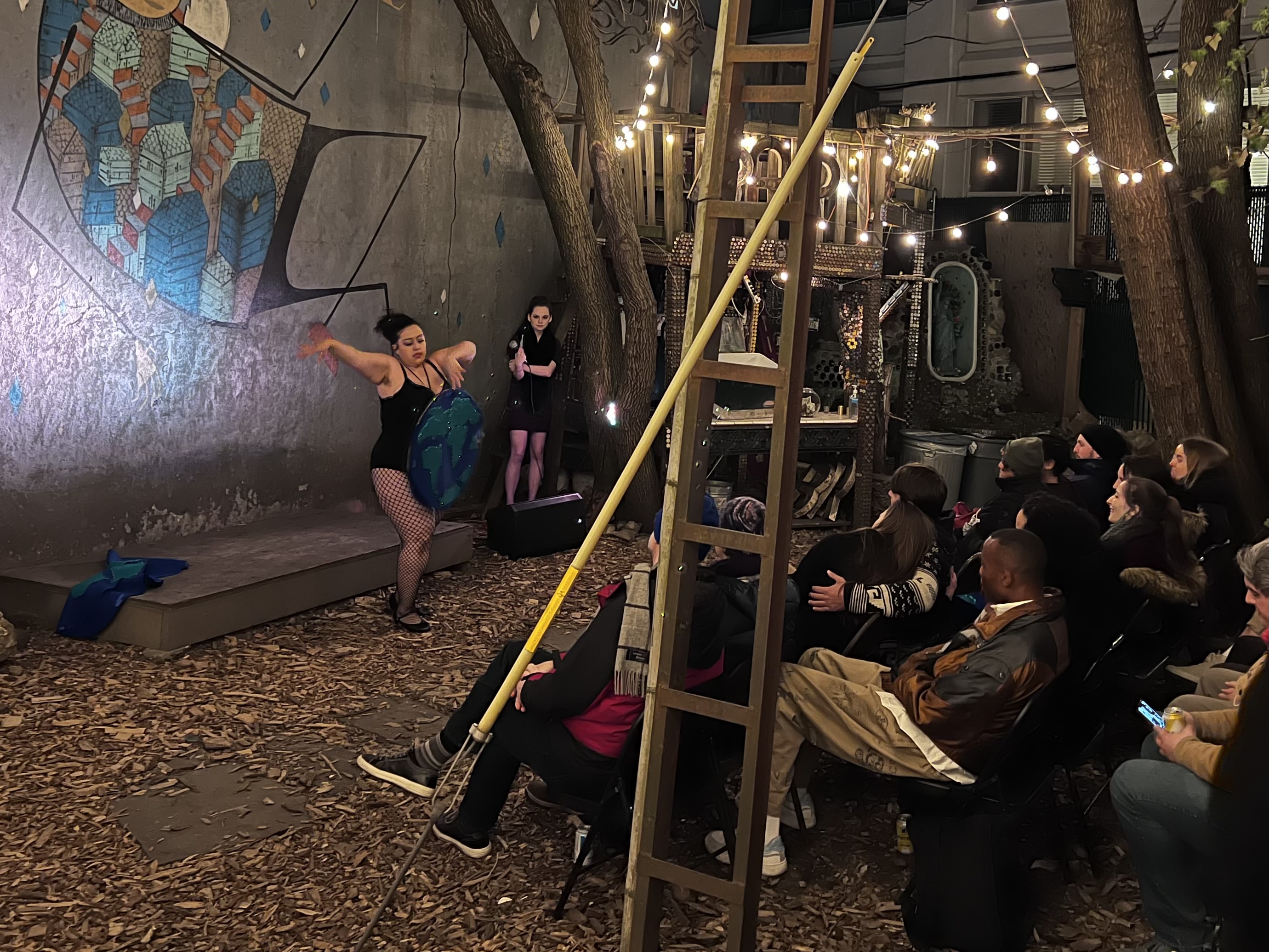 a burlesque dancer wearing a globe costume dances in front of a backyard crowd