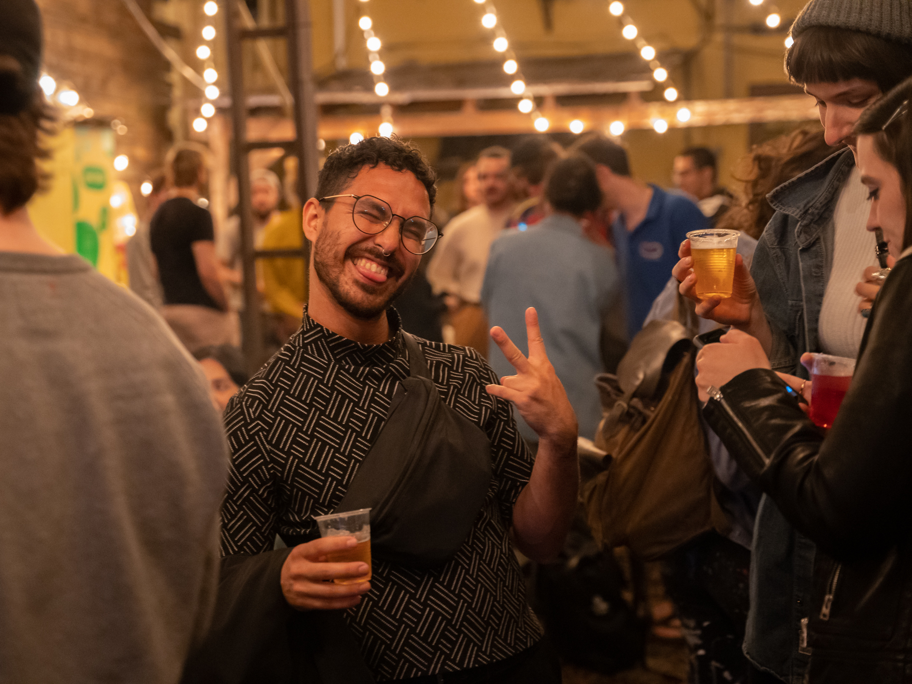 a man smiles at the camera holding a peace sign and a drink