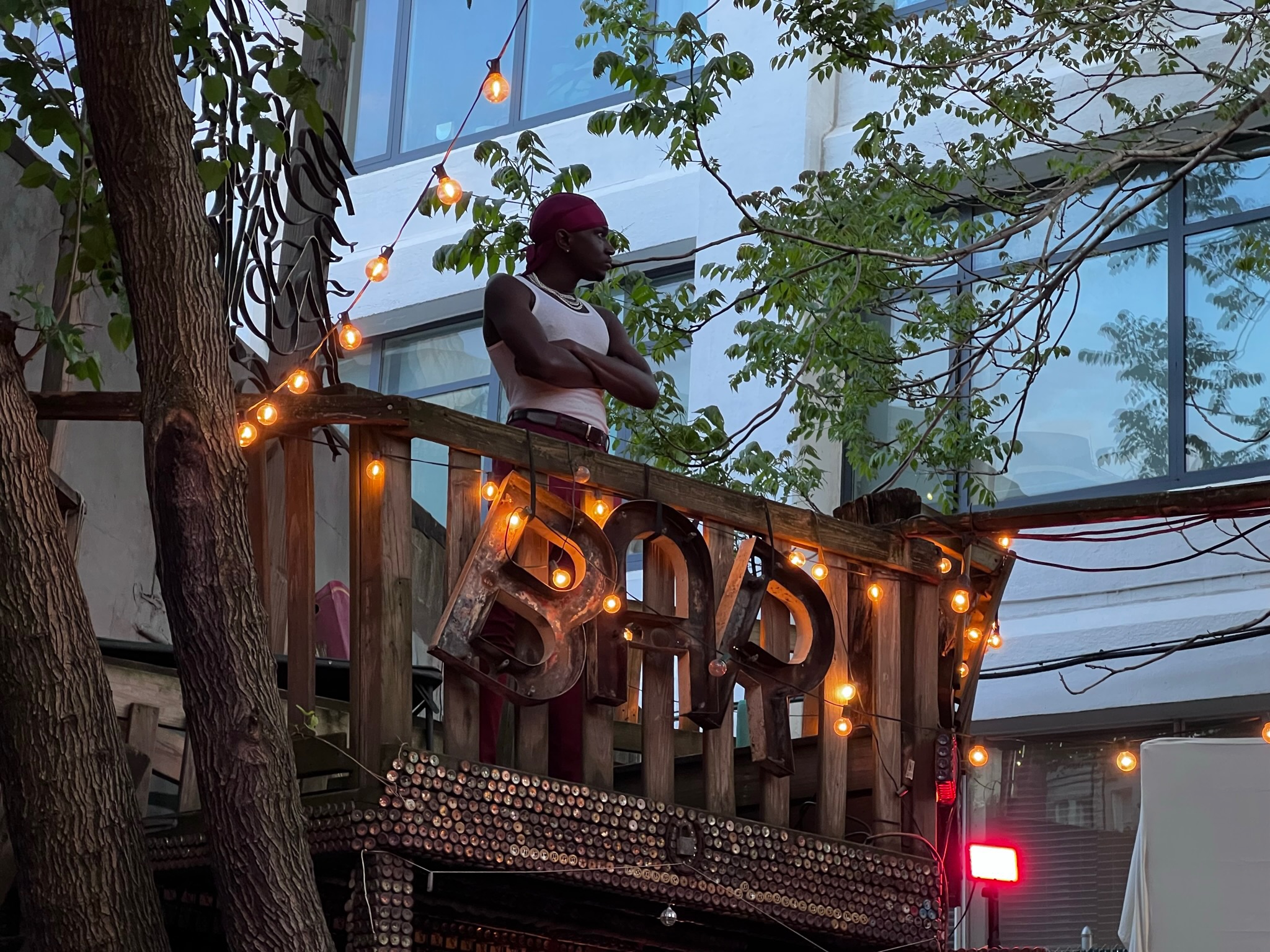 an actor stands atop the bar with arms folded, looking away