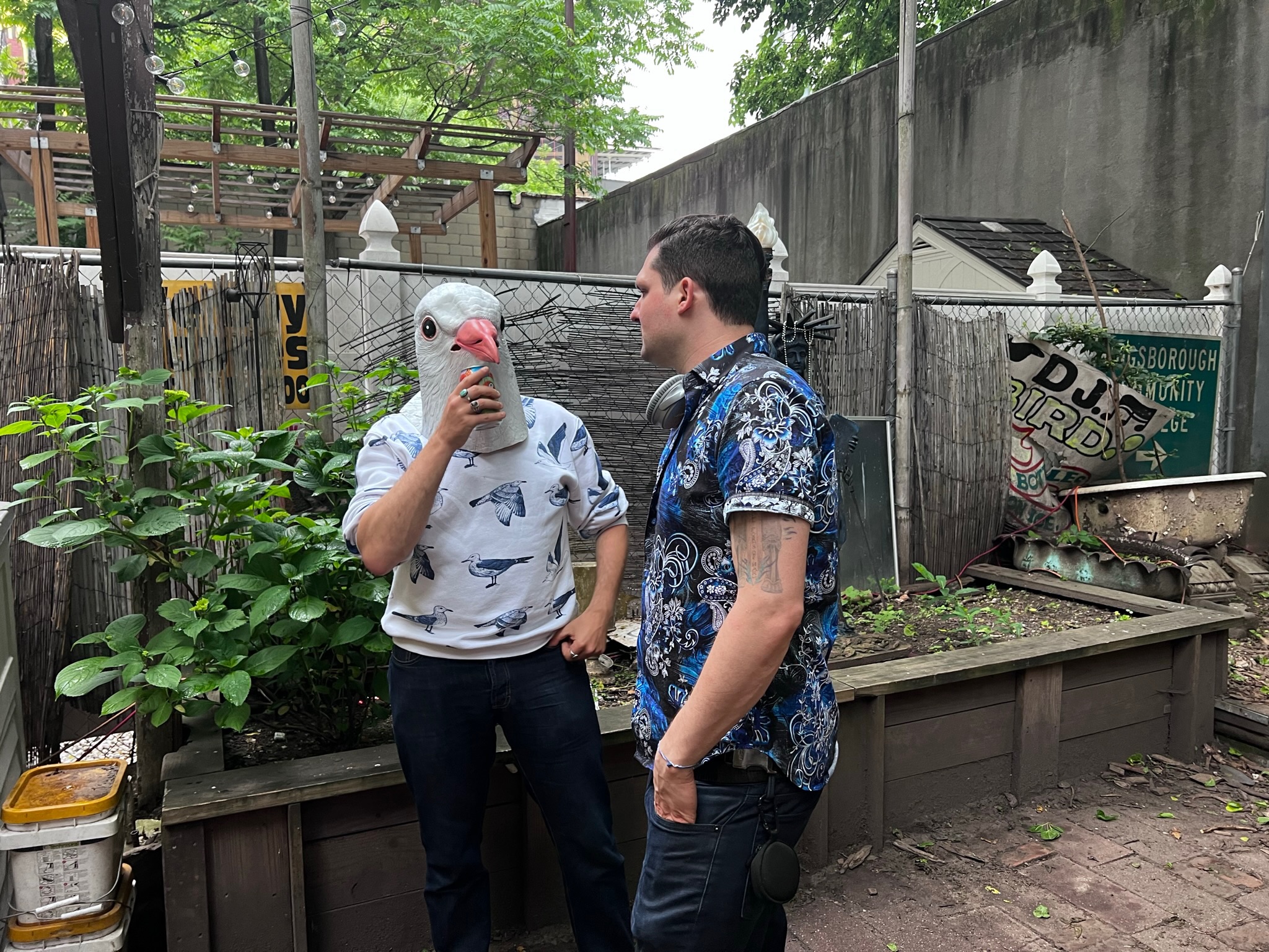 two people converse holding beers, one with a pigeon head